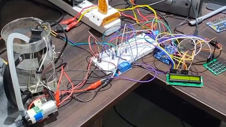 Early prototype on a desk: a glass beaker with probes and tubing running to a small pump motor, a breadboard wired to an Arduino board, an LCD display and a keypad